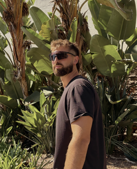A man in dark shield sunglasses standing in front of palm trees