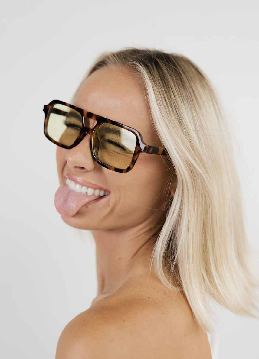 Blonde woman winking in tortoise sunglasses with yellow lenses