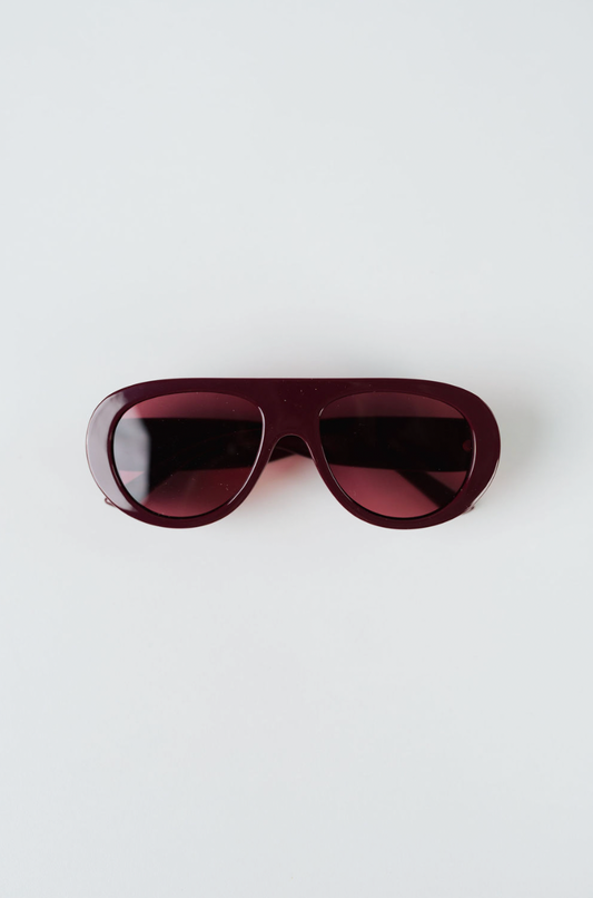 A pair of oversized aviator-style sunglasses with a translucent deep burgundy frame and matching tinted lenses, photographed flat on a light gray background.